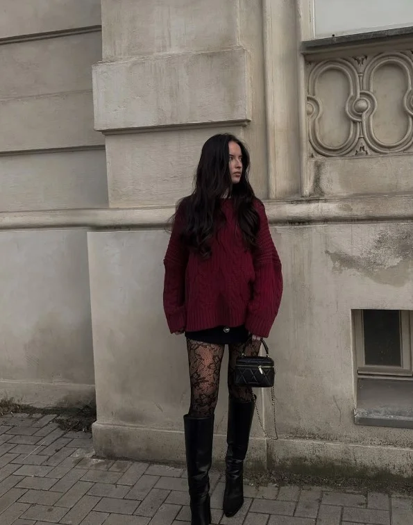 Woman wearing long black boots with dark jeans and a burgundy sweater.