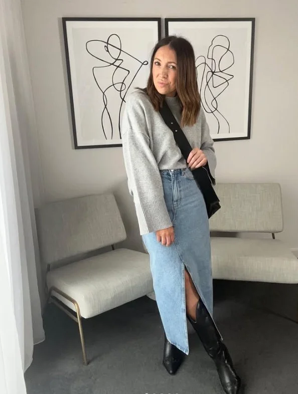 Woman wearing long black boots with a denim midi skirt and a sweater.