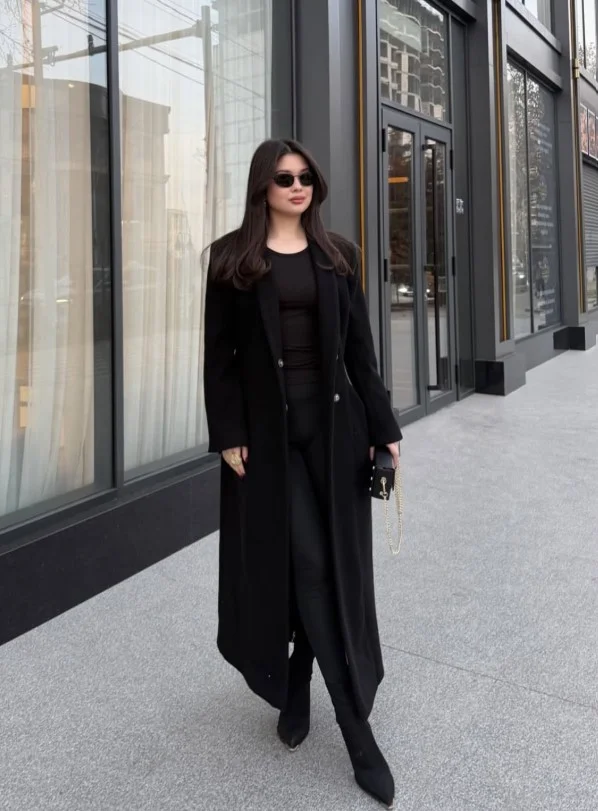 Woman wearing long black boots with black trousers, a black knit sweater, and a long black coat.