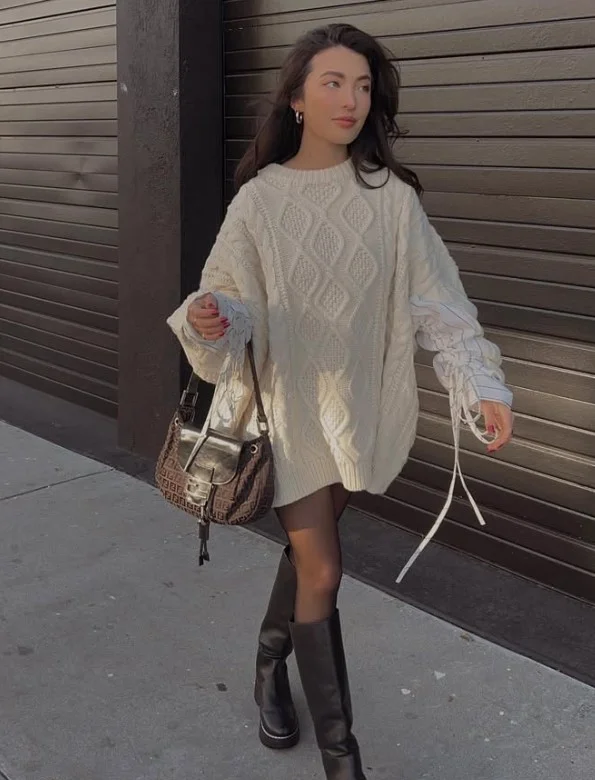 Woman wearing long black boots with black leggings, an oversized sweater, and a long coat.