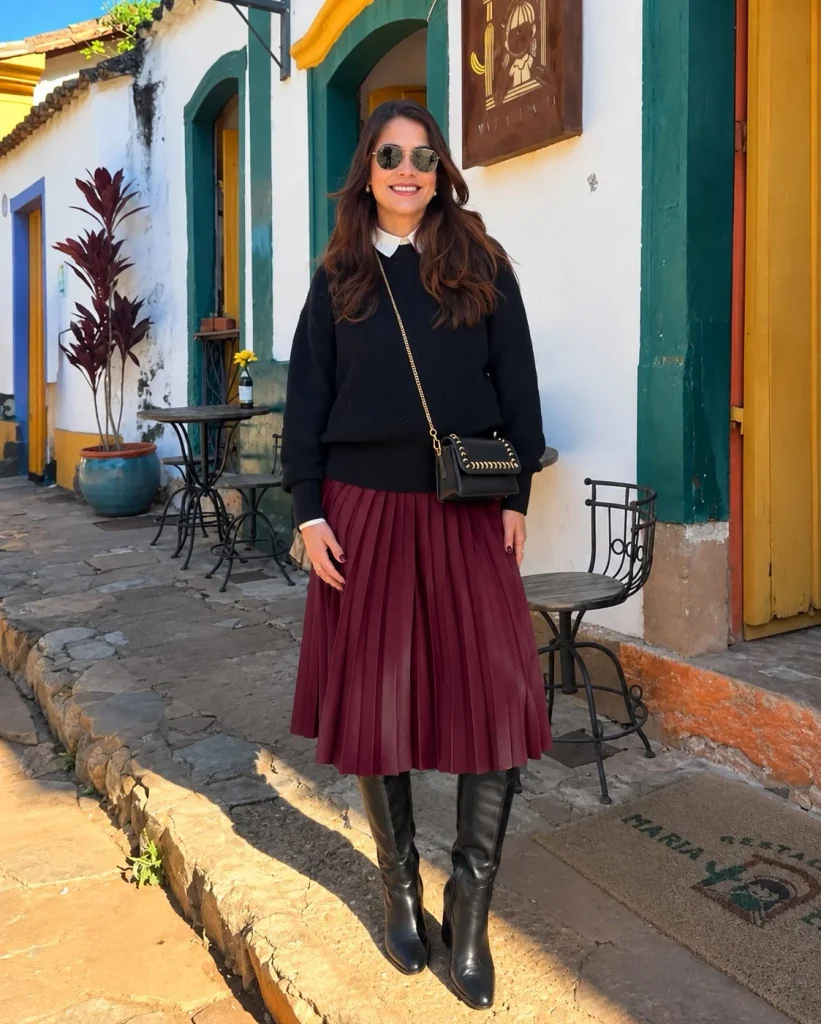 Woman wearing long black boots with a pleated midi skirt, fitted turtleneck, and long coat.