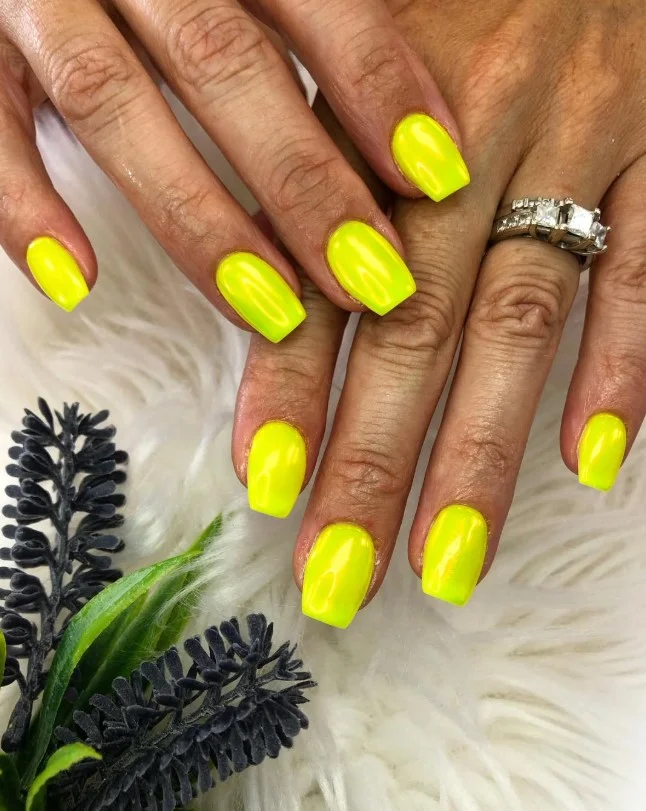 Neon yellow nails creating a vibrant vacation manicure against tan skin.