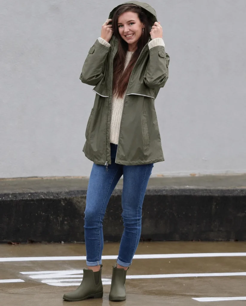 Woman wearing olive short rain boots with blue jeans, a cream knit sweater, and a brown leather bag.