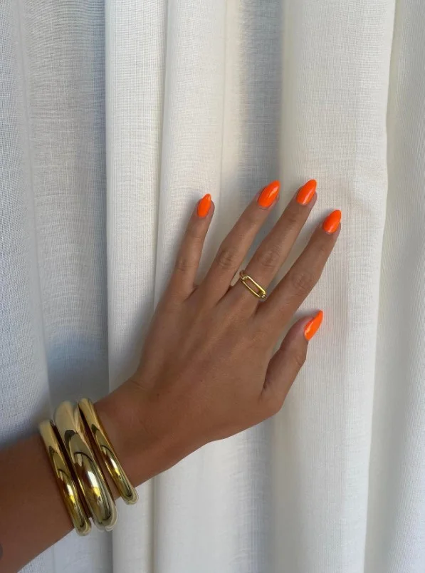 Bright orange nails complementing tan skin for a vibrant sun-kissed manicure.