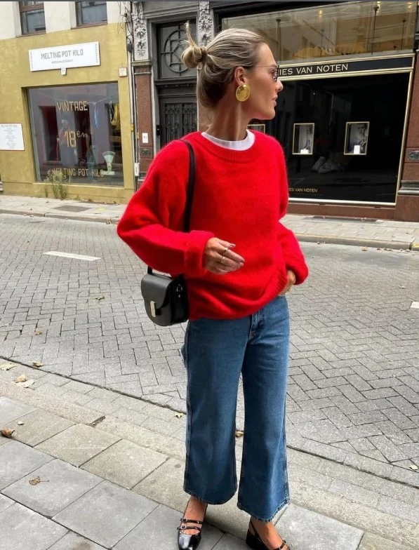 Woman wearing dark blue jeans with a bold red sweater and neutral shoes for a colorful casual outfit.
