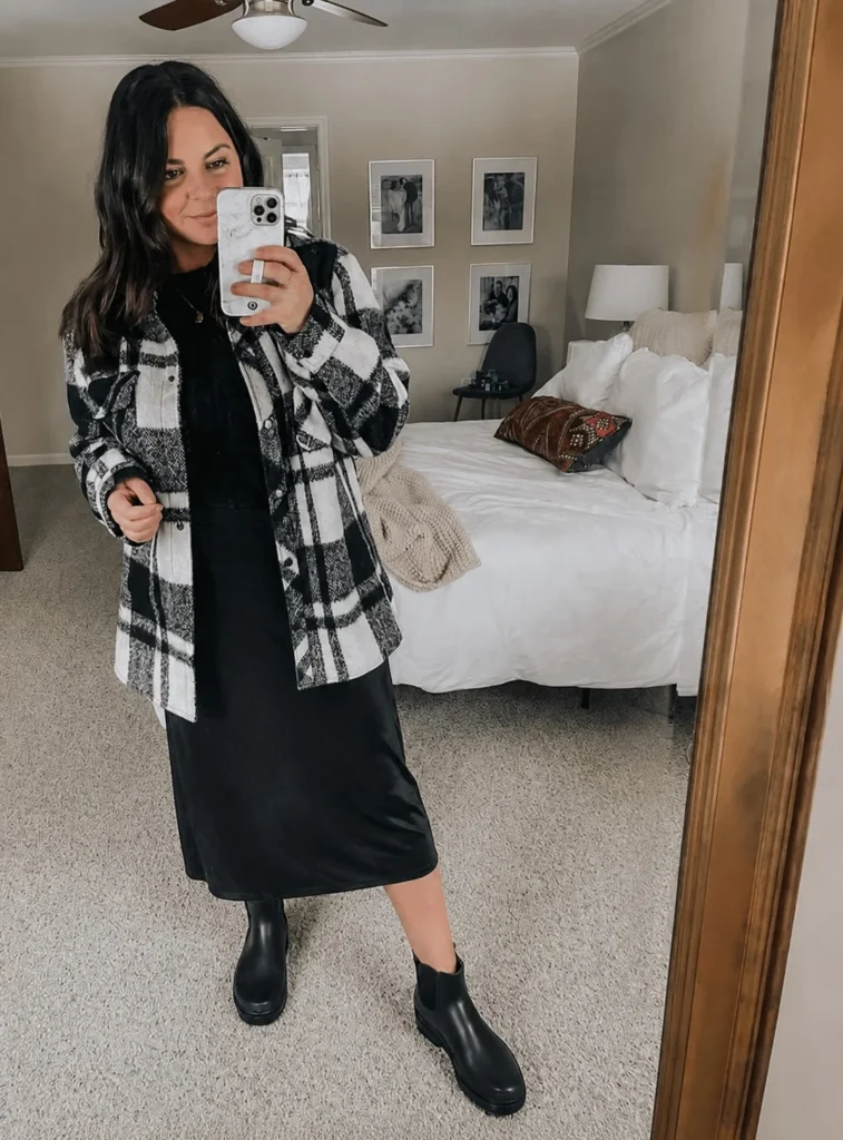Woman wearing short black rain boots with a midi skirt, fitted sweater, and structured coat.
