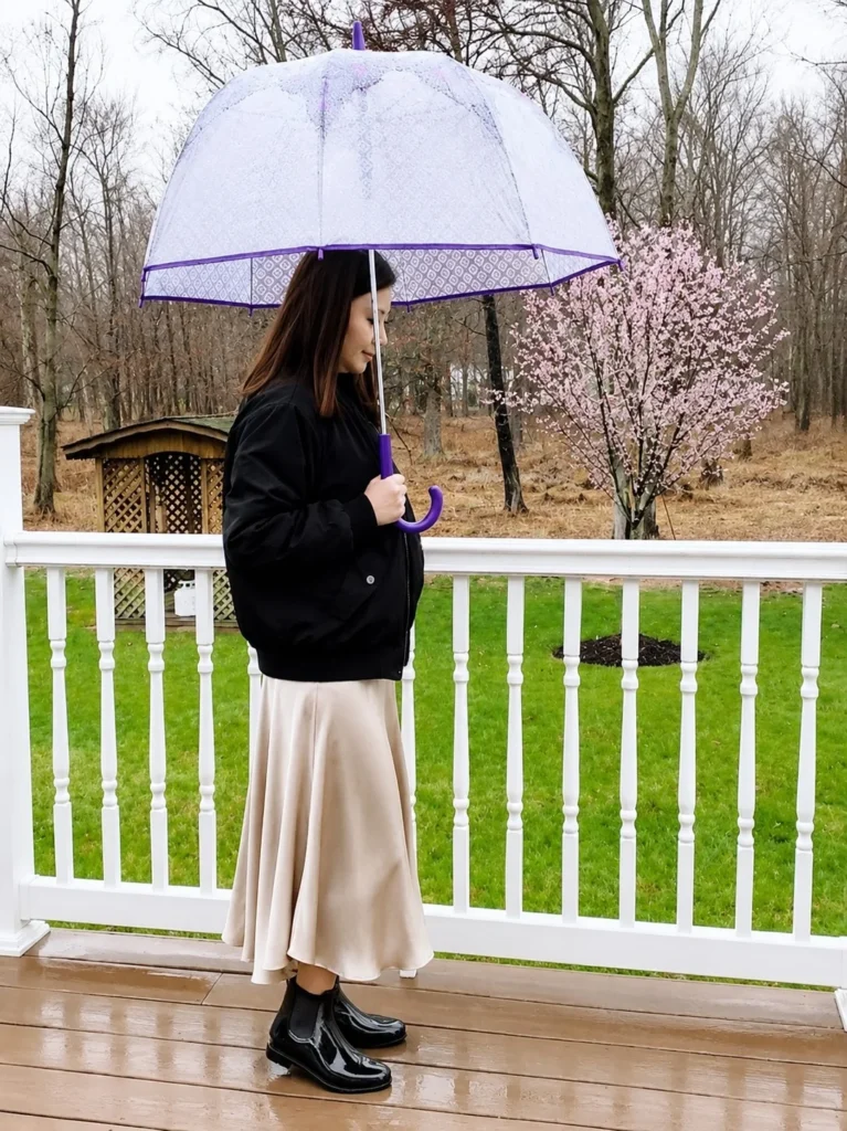 Woman wearing short rain boots with a satin midi skirt, soft cardigan, and structured coat.
