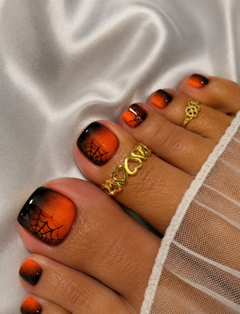 Smoky orange ombre Halloween toe nail designs with delicate black spiderweb artwork.