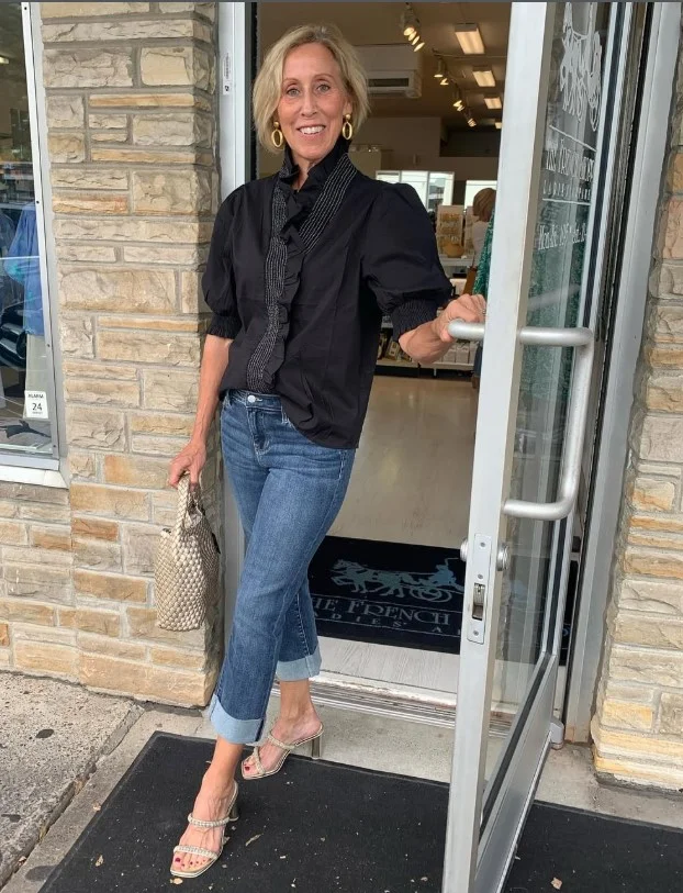 Woman wearing dark blue jeans with a statement blouse, pointed heels, and elegant accessories for a polished evening outfit.
