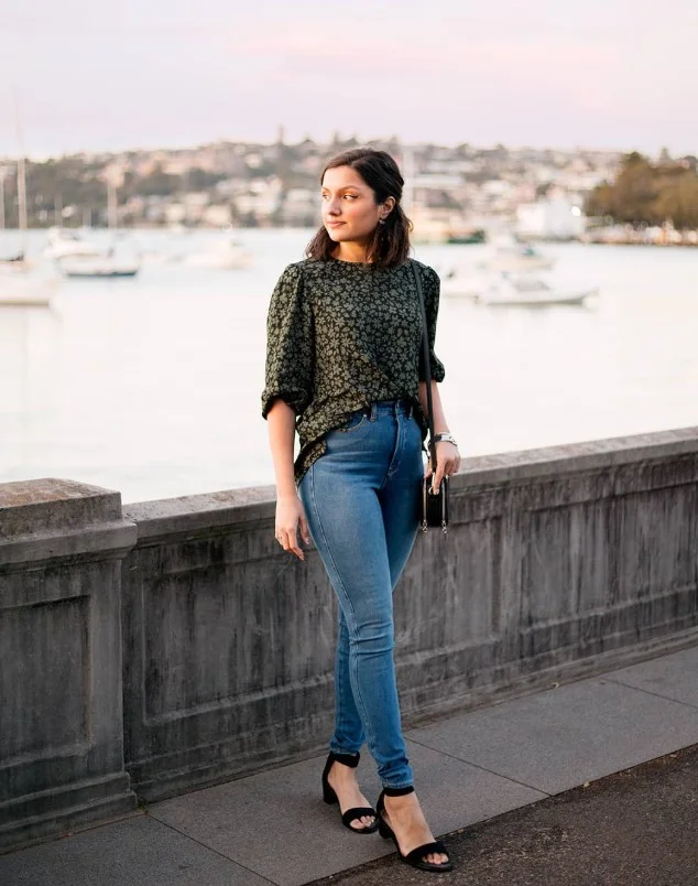 Woman wearing dark blue jeans with a tucked cream blouse, leather belt.