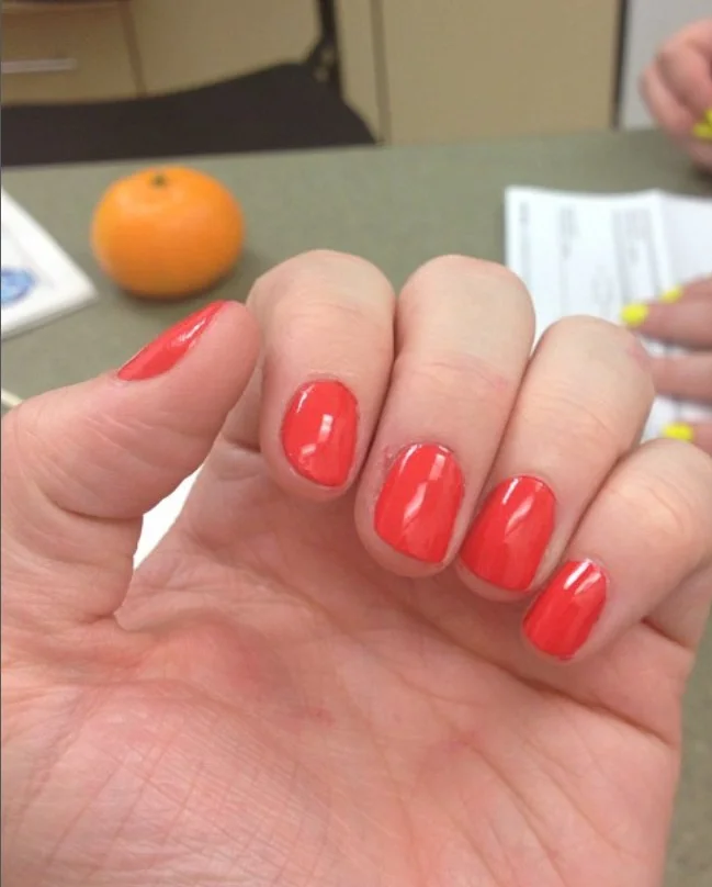 Warm coral nail varnish complementing pale skin with a bright fresh summer manicure.