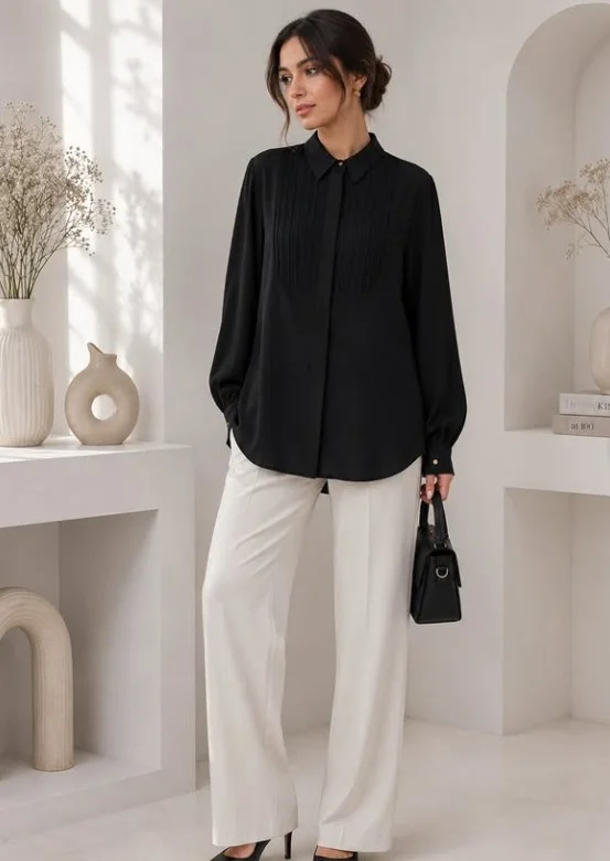 Woman wearing white jeans with a black blouse, black belt, and polished accessories for a chic dinner outfit.