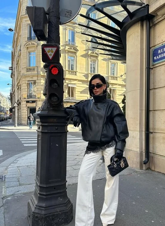 Woman wearing white jeans with a black leather jacket, simple top, and ankle boots for an edgy chic outfit.