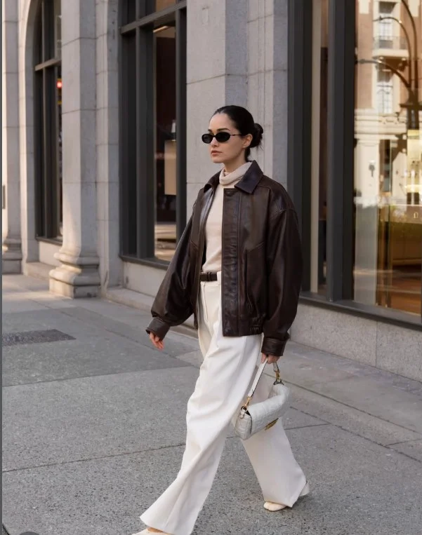 Woman wearing white jeans with a brown leather jacket and simple top for a stylish transitional-season outfit.