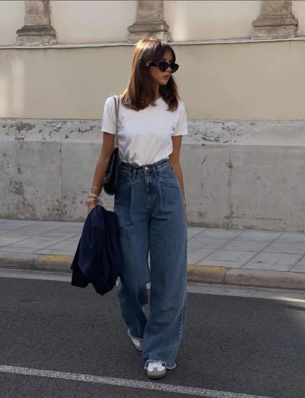 Woman wearing dark blue jeans with a classic white T-shirt, leather belt, and white sneakers.