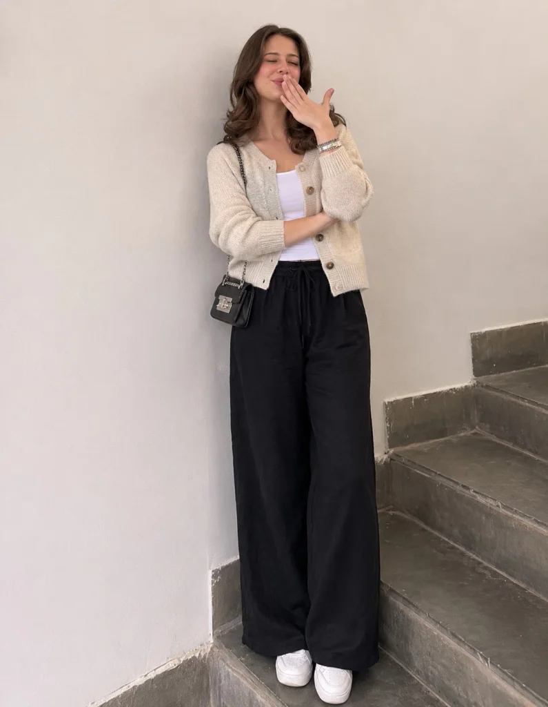 Woman wearing black linen pants with an oatmeal cardigan, fitted top, and white sneakers