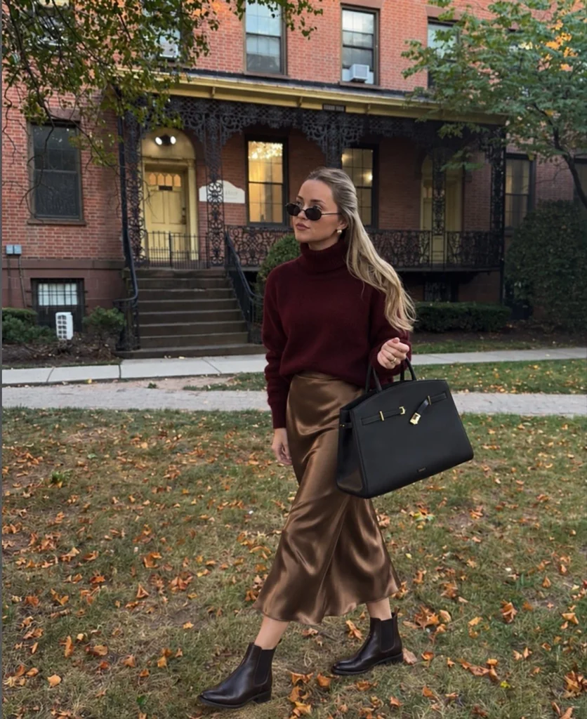 Woman wearing a burgundy turtleneck sweater with a bronze satin midi skirt and Chelsea boots