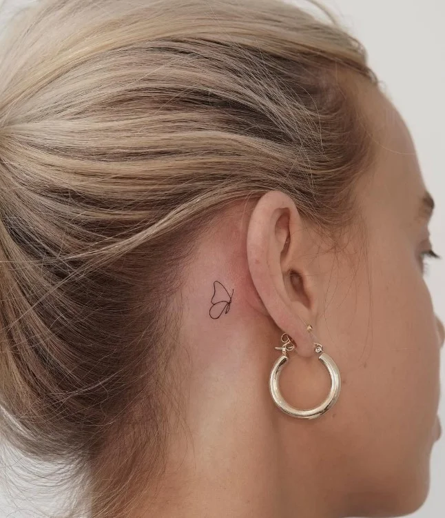 Delicate butterfly behind the ear tattoo for women with simple fine-line details