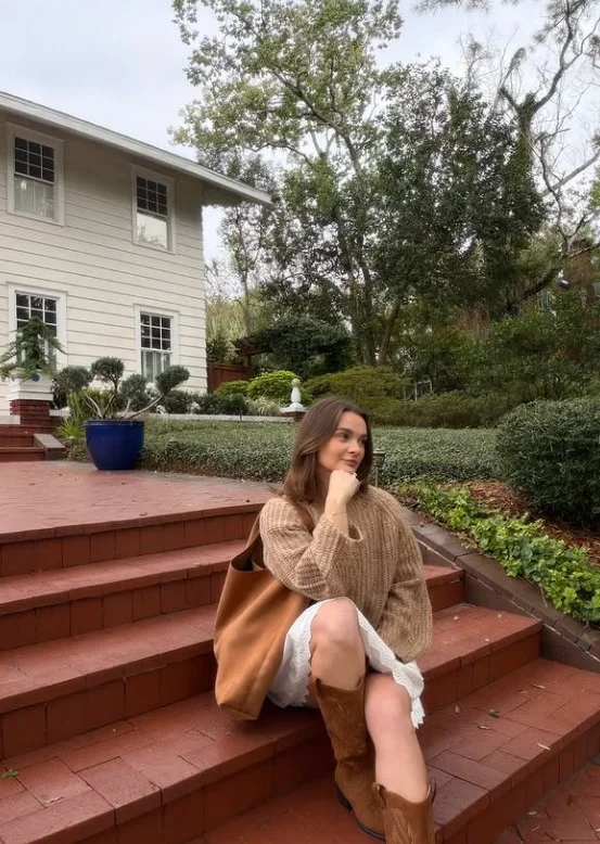 Woman wearing a chocolate brown sweater with an ivory A-line midi skirt and knee-high boots