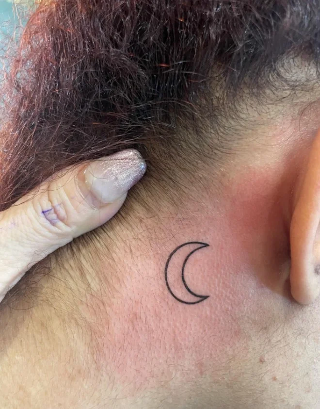Crescent moon behind the ear tattoo with a simple delicate design