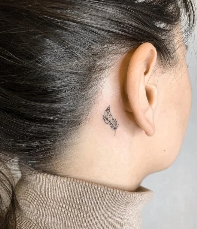 Small feather behind the ear tattoo with a delicate fine-line design