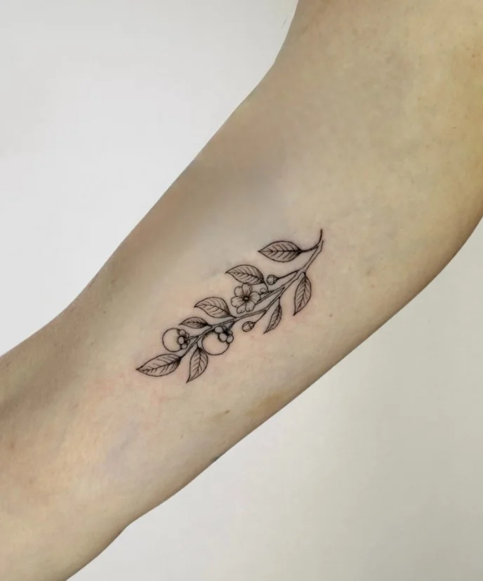 Fine-line botanical branch forearm tattoo with delicate leaves and flowers