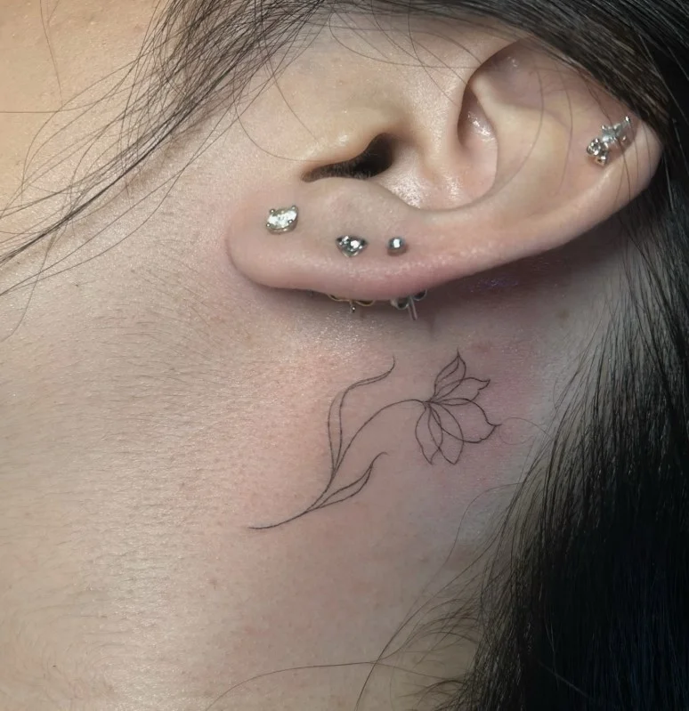 Fine-line floral behind the ear tattoo with a delicate single flower design