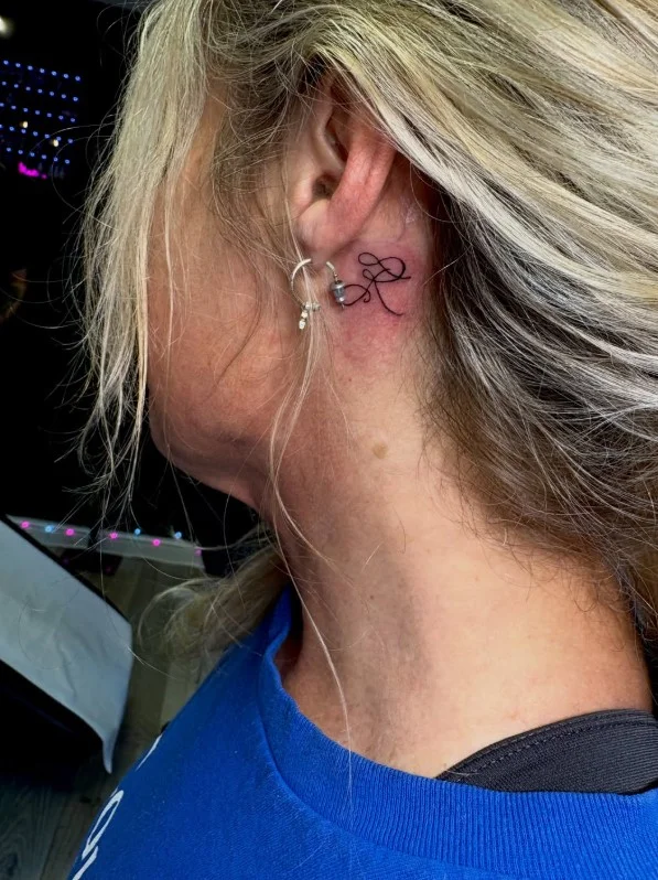 Initial behind the ear tattoo with a simple elegant letter design
