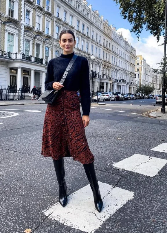 Woman wearing a midi skirt, chunky knit sweater, and black pointed ankle boots