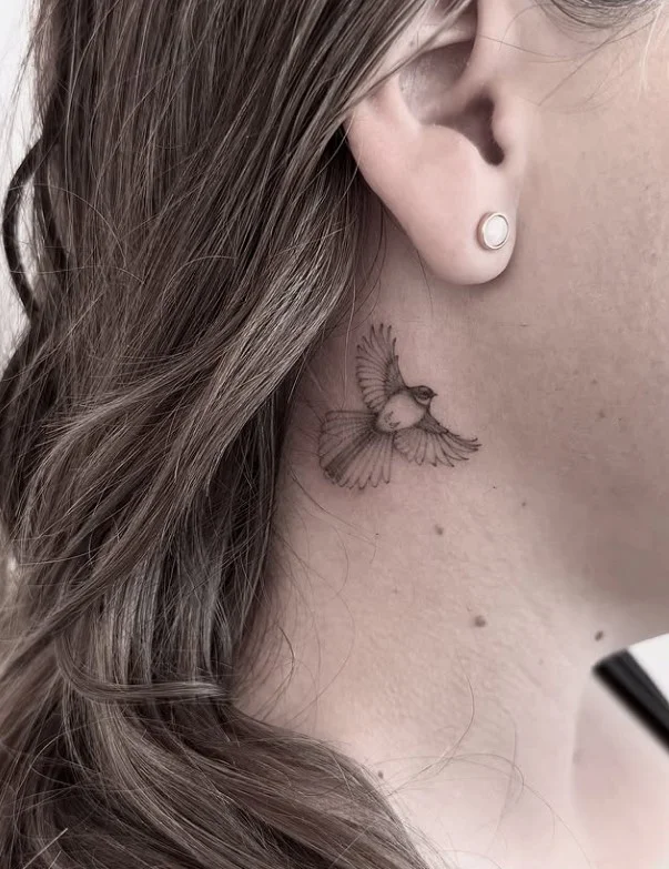 Small bird behind the ear tattoo with a simple delicate outline