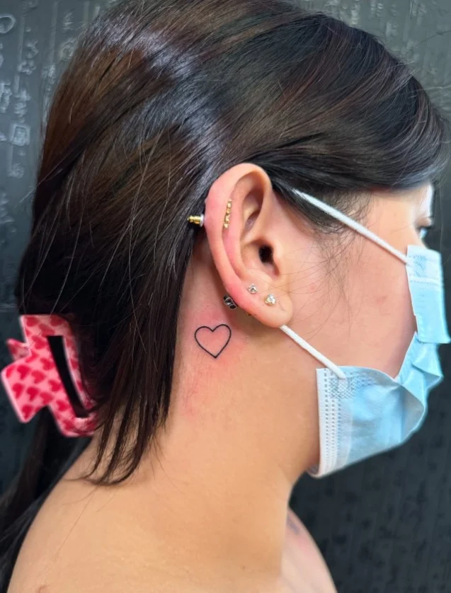 Tiny heart behind the ear tattoo with a simple fine-line design