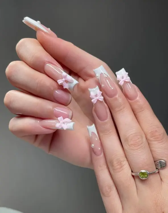 Pink acrylic nails decorated with raised white 3D bows in a delicate coquette style.