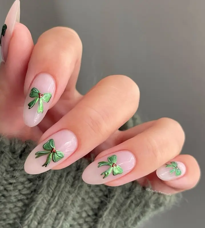 Baby pink Christmas nails decorated with delicate green bows and fine ribbon tails