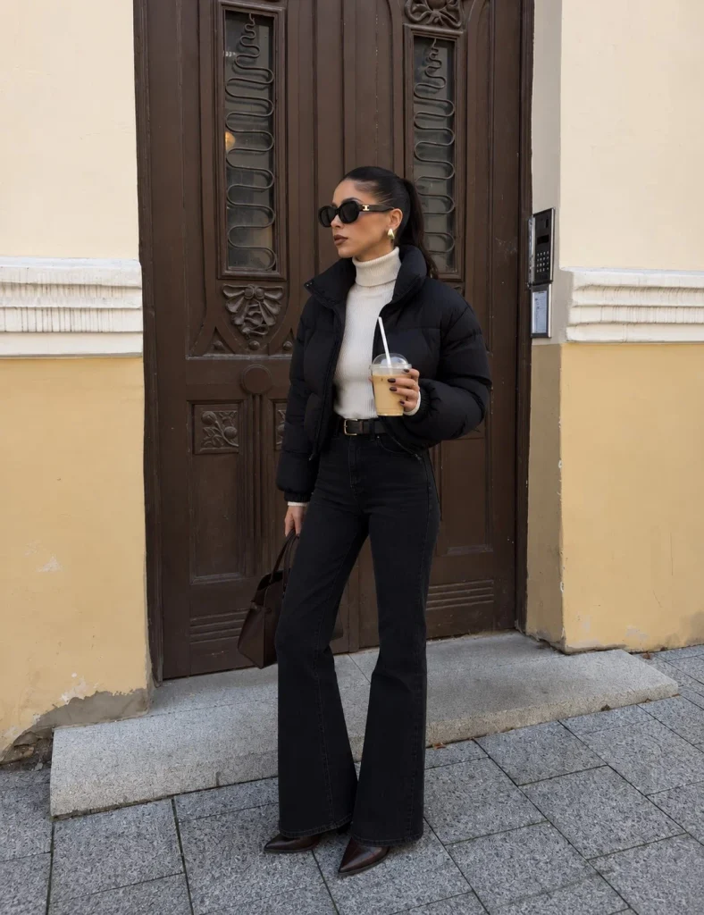Black cropped puffer jacket with black flared jeans, cream sweater and pointed Western boots