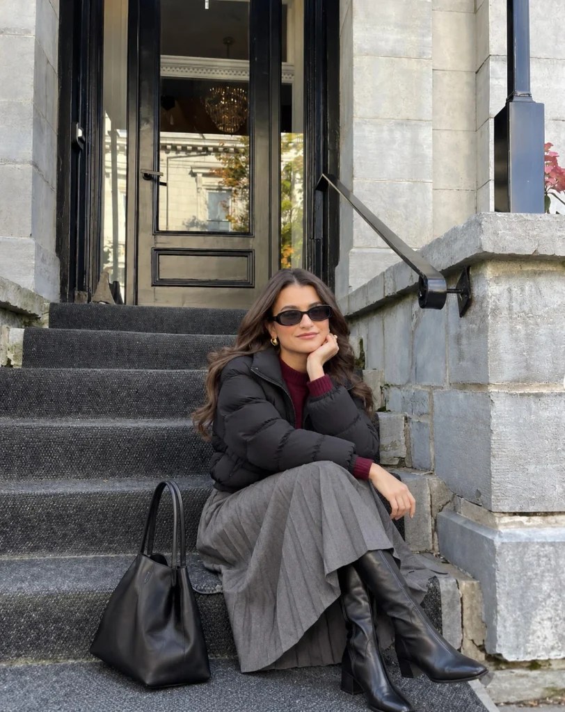 Black cropped puffer jacket with pleated midi skirt, burgundy sweater and black knee-high boots