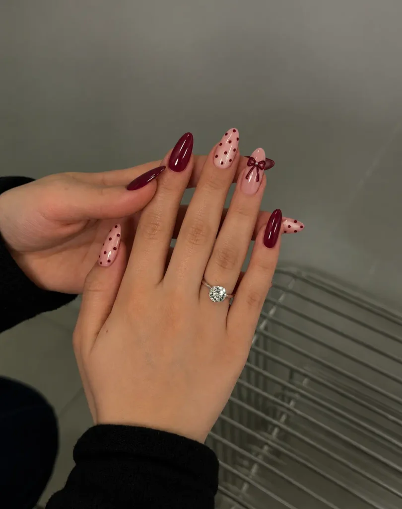 Pink nails with burgundy polka dots and a burgundy bow accent