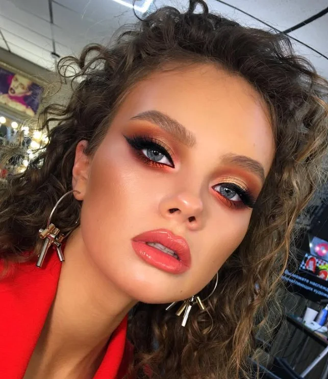 Woman wearing bright coral lipstick with warm pink-orange tones on brown skin