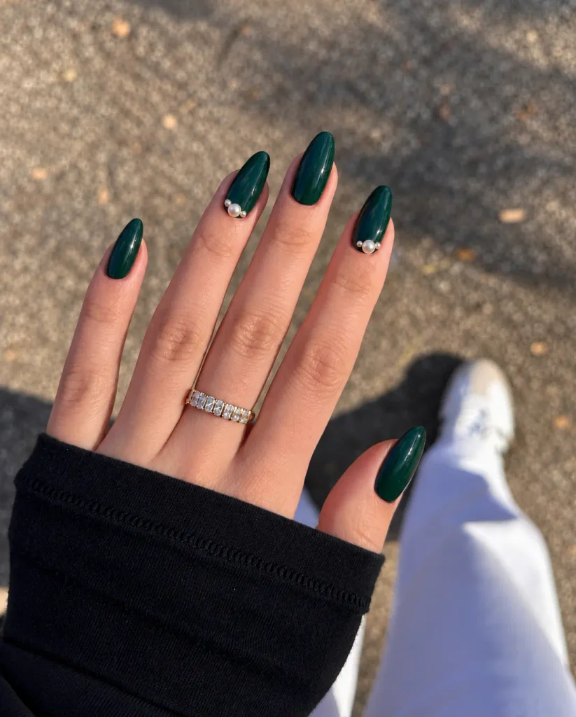 Dark green Christmas nails decorated with small pearl accents near the cuticles or clustered on an accent nail