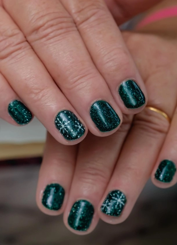Dark green glitter Christmas nails decorated with delicate white snowflake nail art