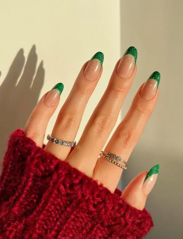 Green glitter Christmas French tip nails with sparkling green tips over a nude pink base