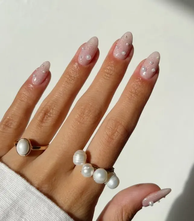 Nude acrylic nails decorated with small pearl accents near the cuticles.