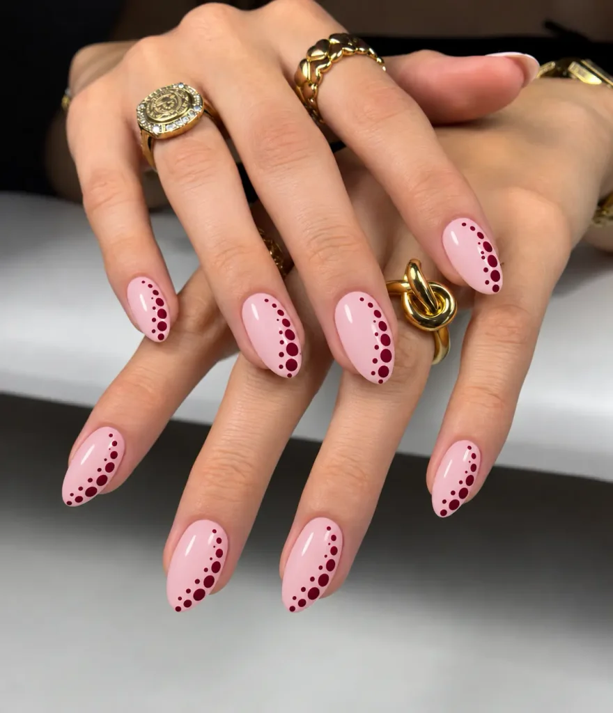 Pink nails with burgundy polka dots arranged in a curved diagonal pattern