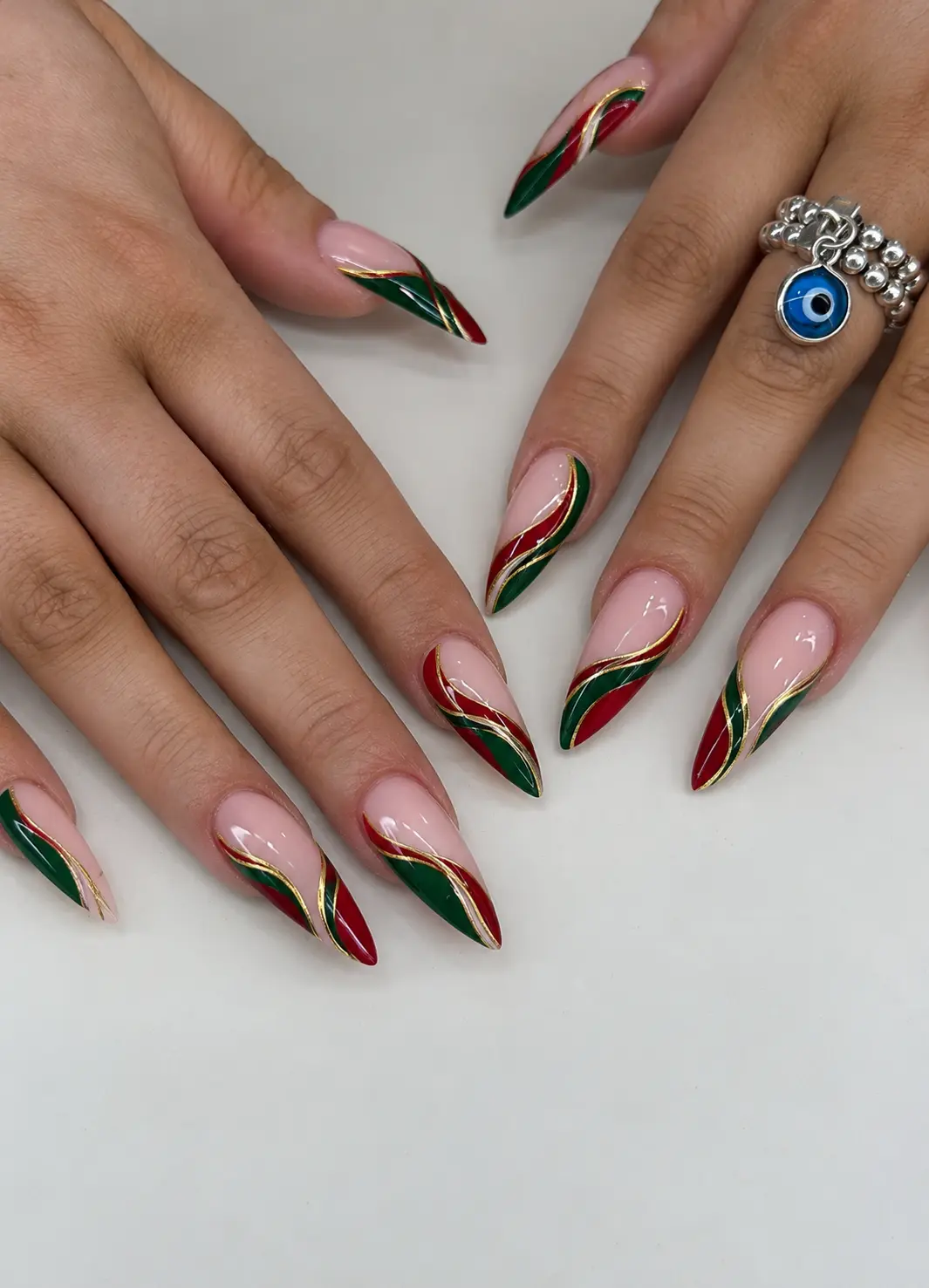 Red and green Christmas swirl nails with flowing color curves and thin gold chrome lines