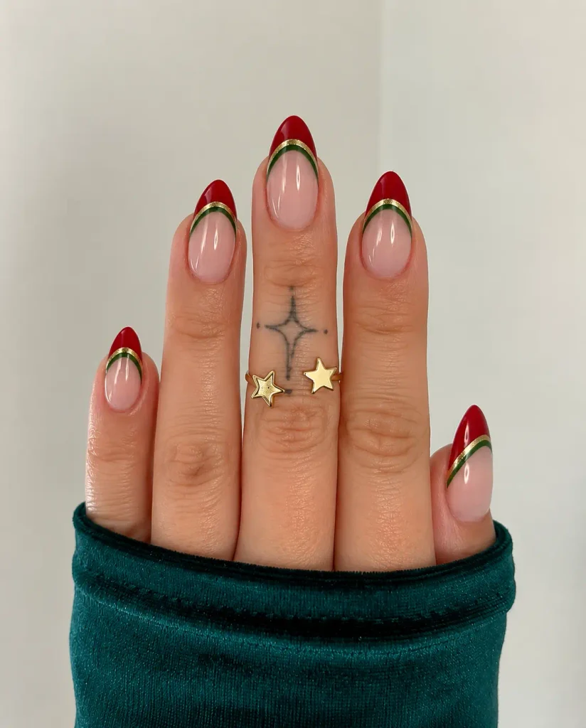 Red Christmas French tip nails with green outlines and thin gold trim on an almond-shaped manicure